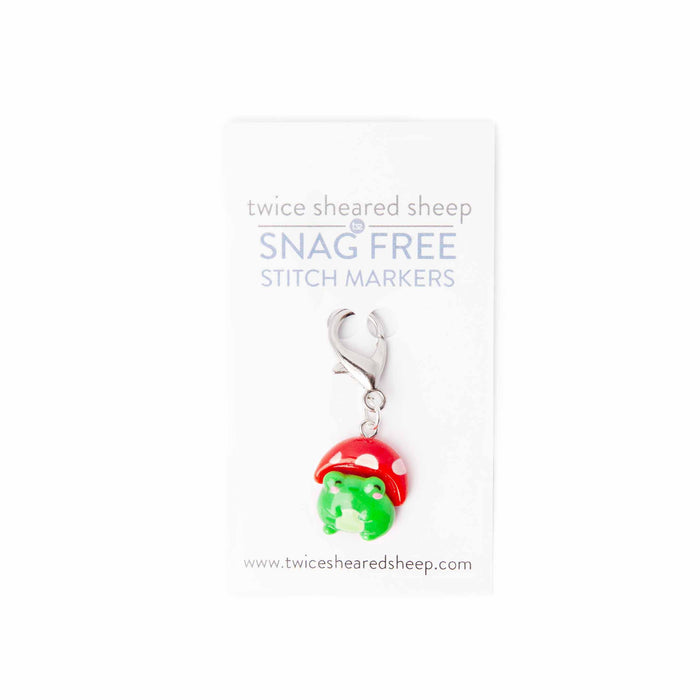 Close-up of mushroom hat frog clip stitch marker on Twice Sheared Sheep Snag Free branded card showing the green kawaii frog wearing a red polka-dot mushroom cap with lobster clasp