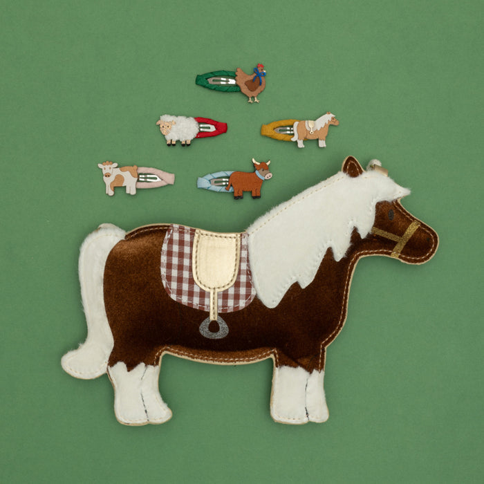 A set of small farm-themed hair clips arranged on a solid green background, with a larger embroidered brown and white horse piece in the foreground. The smaller clips include a cow, sheep, chicken, horse, goat, and bull.