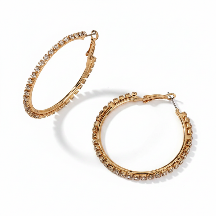Pair of gold-tone hoop earrings encrusted with shimmering pavé crystals, shown on a clean white background with soft shadows for a luxury boutique aesthetic.