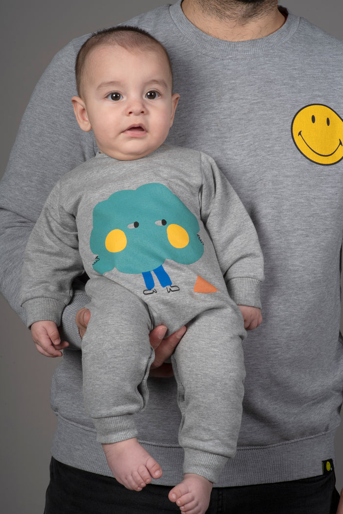 a baby being held wearing grey romper with colorul tree graphic