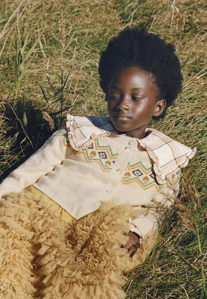 Child sitting on the grass wearing a patterned Cardigan