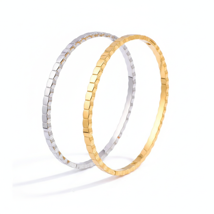 Two interlocking textured bangles, one silver and one gold, featuring a modern geometric faceted design on a white background.