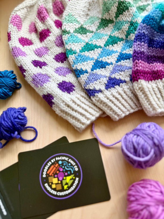 Three Geometric Doodle colorwork hats in purple, teal and pink diamond patterns