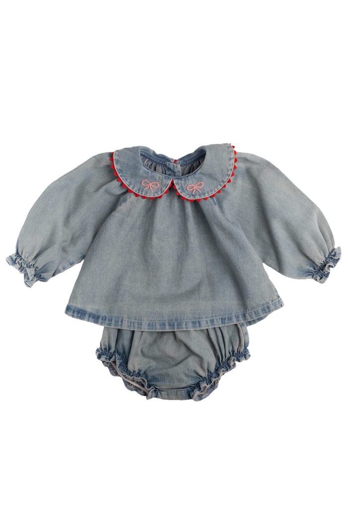 A baby girl's denim two-piece outfit featuring a long-sleeve top with a Peter Pan collar trimmed in red and a matching ruffled bloomers, laid flat on a white background.