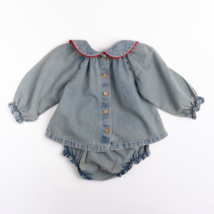 A baby girl's denim set in a faded blue wash, featuring a Peter Pan collar with red trim, buttoned front, and ruffled cuffs and leg openings, laid flat on a white background.