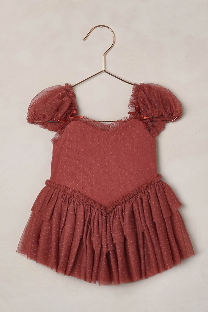 Red dress with ruffled sleeves on a hanger against a beige background