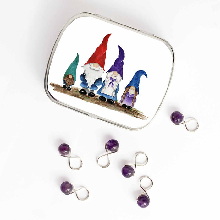 Small hinged Gnome Family tin with watercolor gnome family lid, shown beside six purple beaded stitch markers