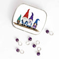 Small hinged Gnome Family tin with watercolor gnome family lid, shown beside six purple beaded stitch markers