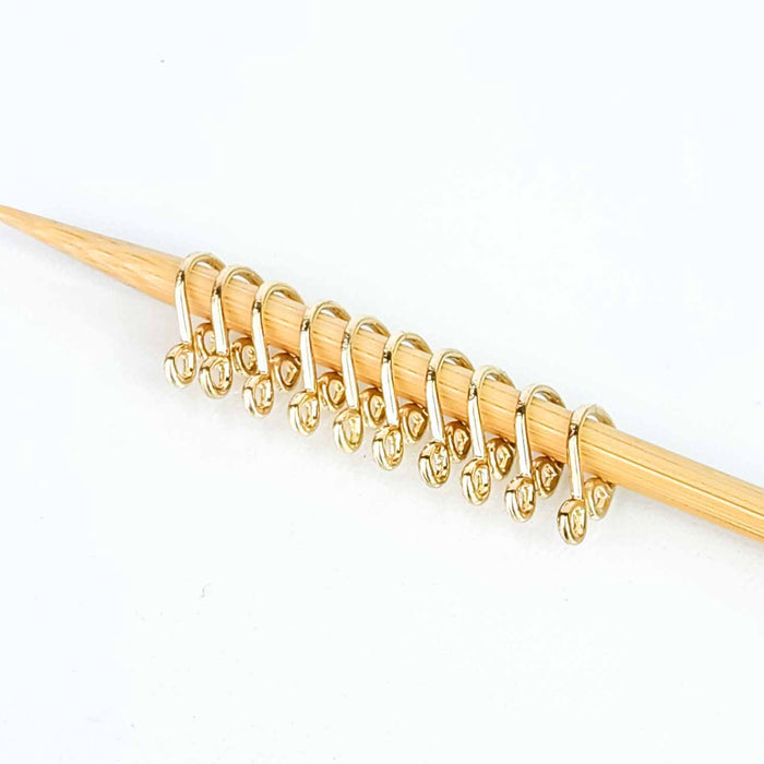 Row of gold cast melody clip stitch markers lined up on bamboo knitting needle