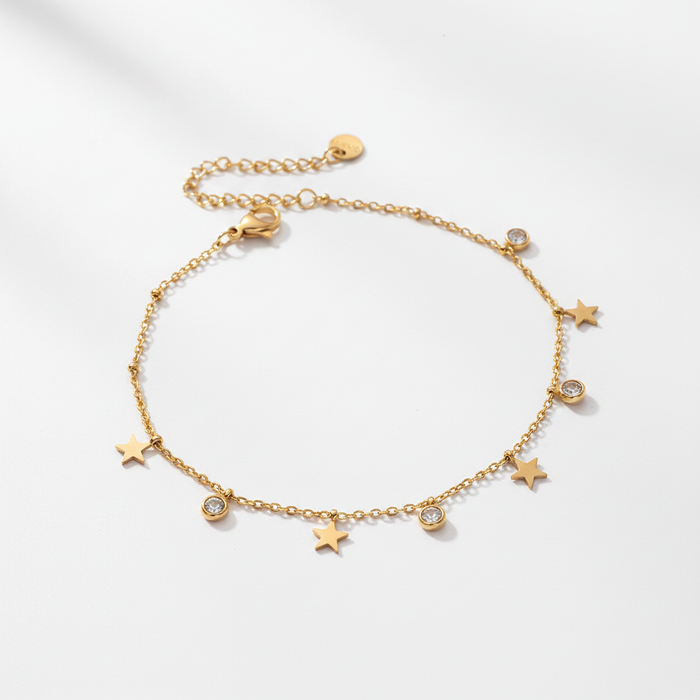 A high-resolution product shot of a gold chain anklet featuring alternating small gold star charms and bezel-set sparkling crystals, displayed on a clean white surface with soft shadows.