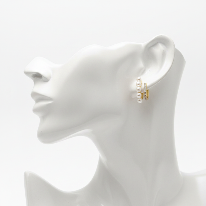 A high-resolution product shot of gold-toned hoop earrings featuring a unique double-band design; one band is lined with small white pearls and the other is pavé-set with sparkling crystals, displayed on a white mannequin bust.