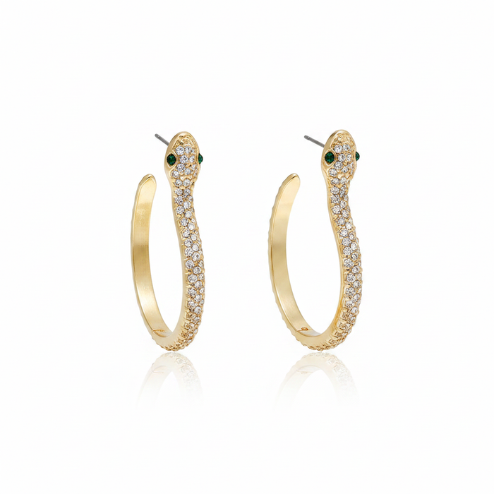 A pair of elegant 18k gold-plated snake hoop earrings featuring shimmering white crystal pavé and striking green emerald-style eyes on a white reflective background.