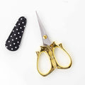 Golden cat embroidery scissors with cat-shaped handles open next to a black and white polka dot blade cover