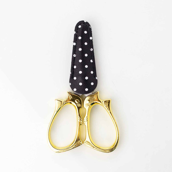 Golden cat embroidery scissors with blades tucked into the black and white polka dot blade cover showing the cat face handles