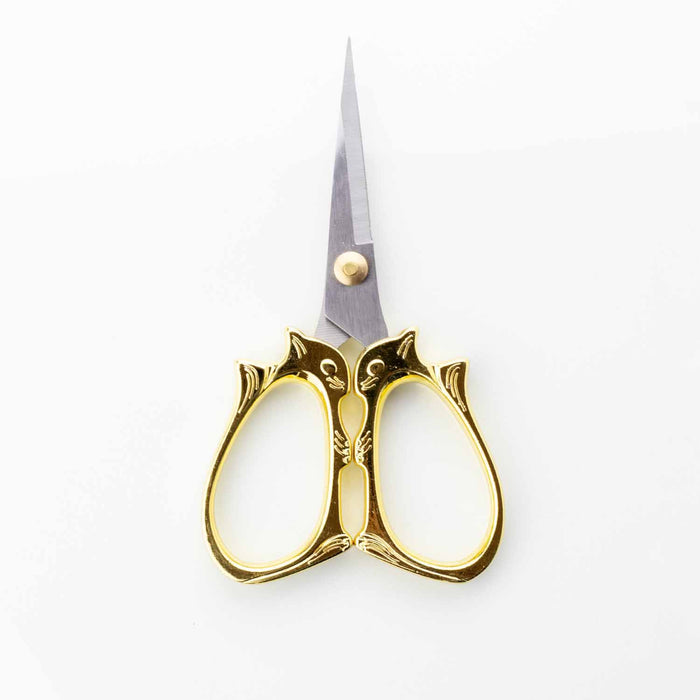 Golden cat embroidery scissors standing upright with blades pointing up showing the detailed cat face design on the handles