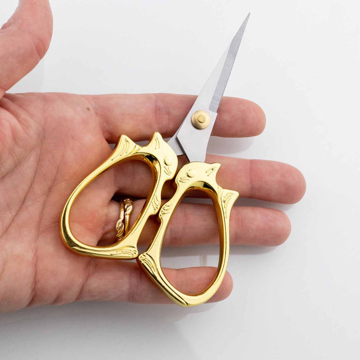 Hand holding the golden cat embroidery scissors to show the compact size and cat face handle detail