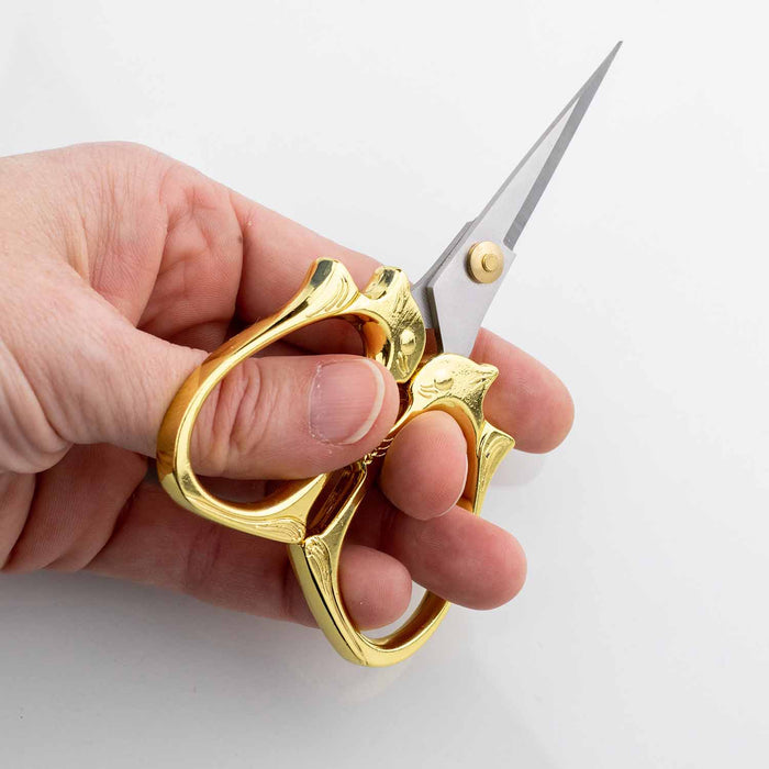 Hand gripping the golden cat embroidery scissors in cutting position to demonstrate comfortable use