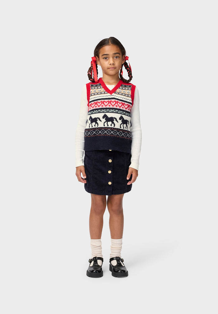 Young girl wearing a patterned sweater vest and skirt on a white background