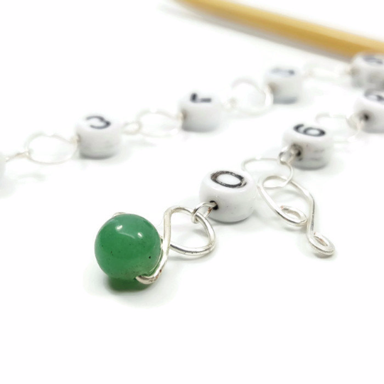 Close-up of green aventurine gemstone bead on silver wire row counter chain with numbered beads on bamboo knitting needle
