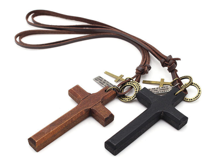 Two large, minimalist wooden cross pendants—one in a natural dark brown wood and one in a matte black finish—featuring smaller bronze-tone metal cross charms and textured brown leather-style cords.