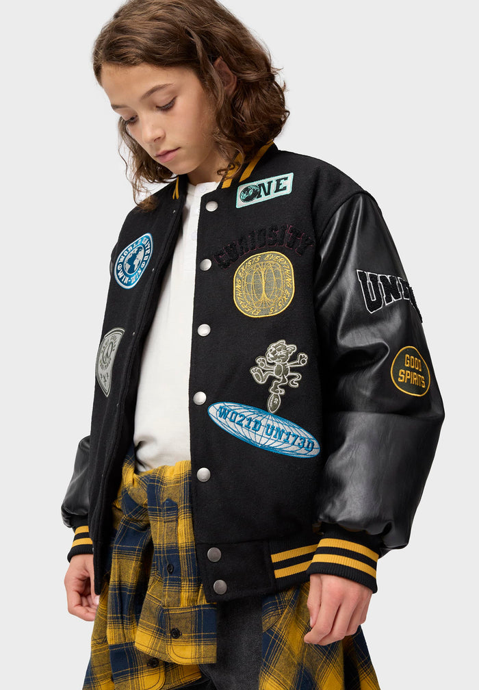 Child wearing a black varsity jacket with patches on a white background