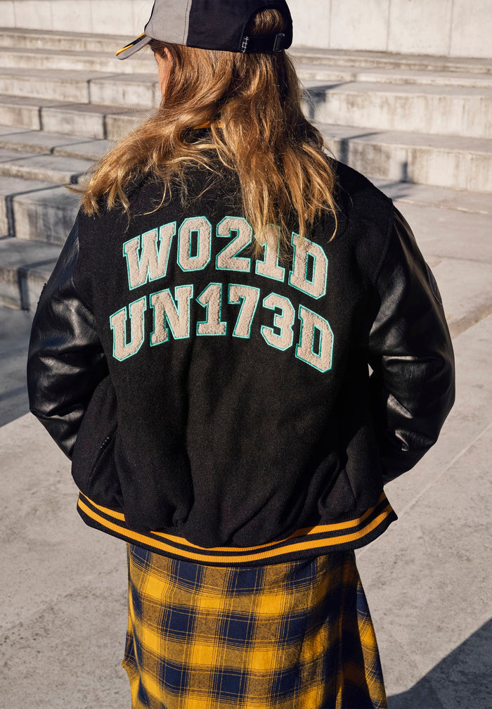 Person wearing a black varsity jacket with standing on stone steps.