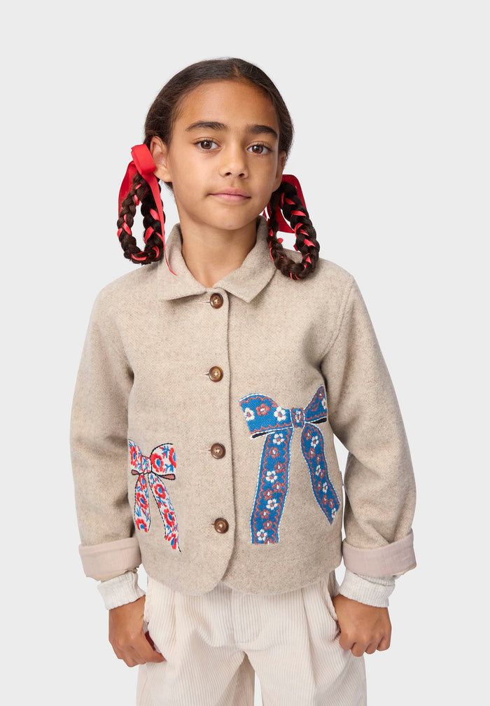 Young girl wearing a beige coat with floral bow designs on a white background