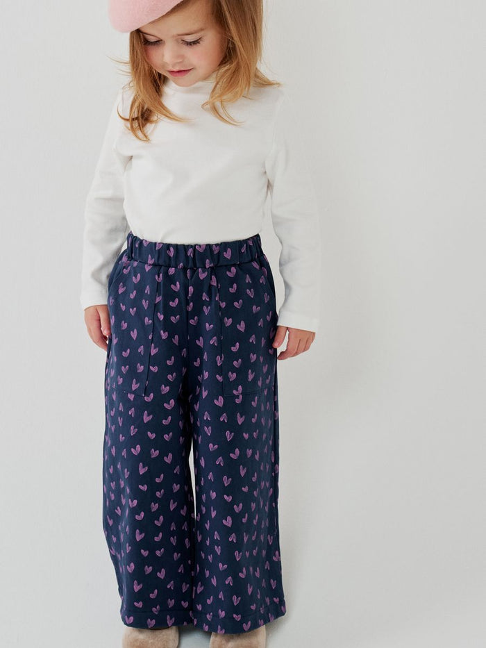 Child wearing a white top and navy pants with pink butterfly pattern on a light gray background