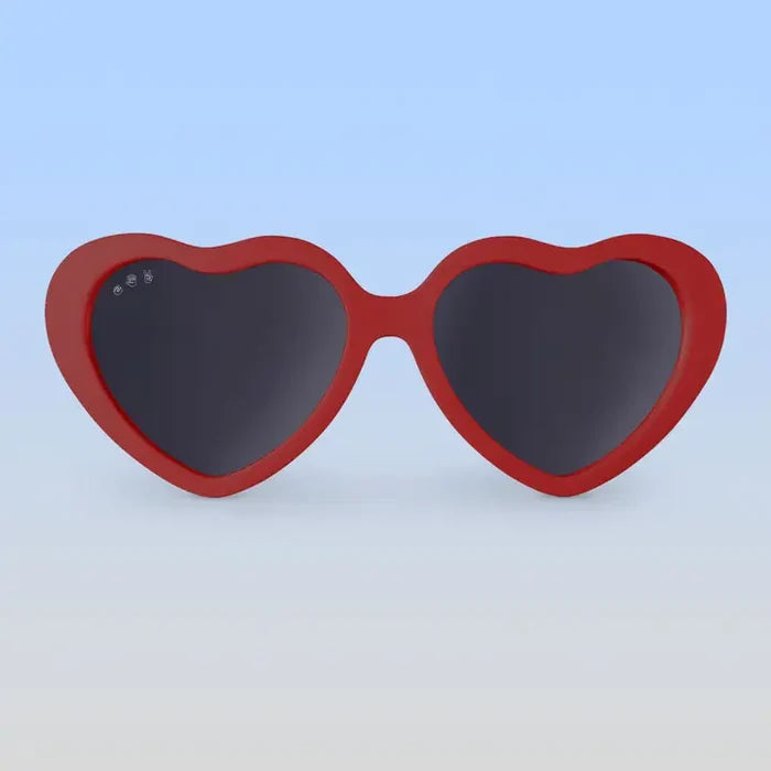 Heart-shaped sunglasses with red frame and dark lenses on a light blue background