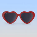 Heart-shaped sunglasses with red frame and dark lenses on a light blue background