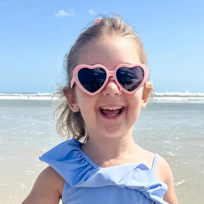 Young girl wearing heart-shaped sunglasses on a beach