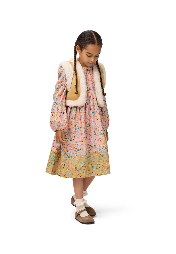 Young girl wearing a floral dress with a fur vest on a white background
