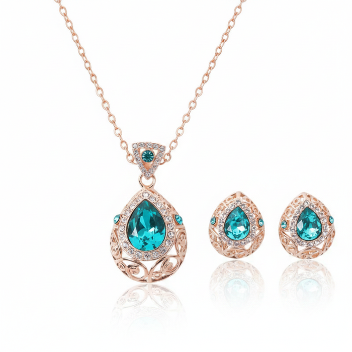 An ornate rose gold jewelry set featuring a teardrop-shaped teal crystal pendant necklace and matching stud earrings with intricate filigree detailing and pavé accents.