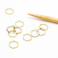 Set of gold hexagonal honeycomb-shaped simple stitch markers scattered on a white surface next to a bamboo knitting needle