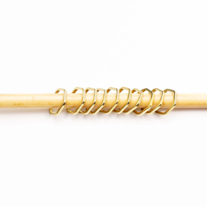 Gold hexagonal honeycomb stitch markers lined up on a bamboo knitting needle showing the snag-free fit