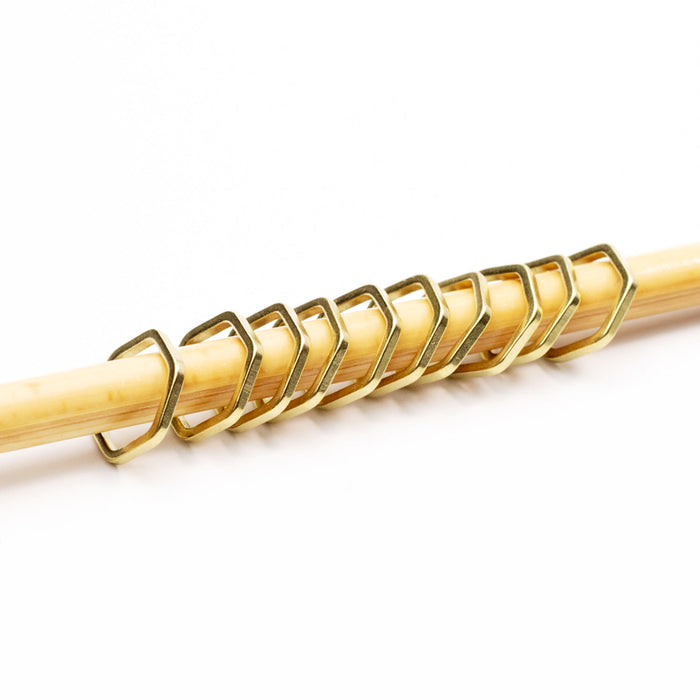 Close-up of gold hexagonal honeycomb stitch markers on a bamboo knitting needle from a slightly angled view