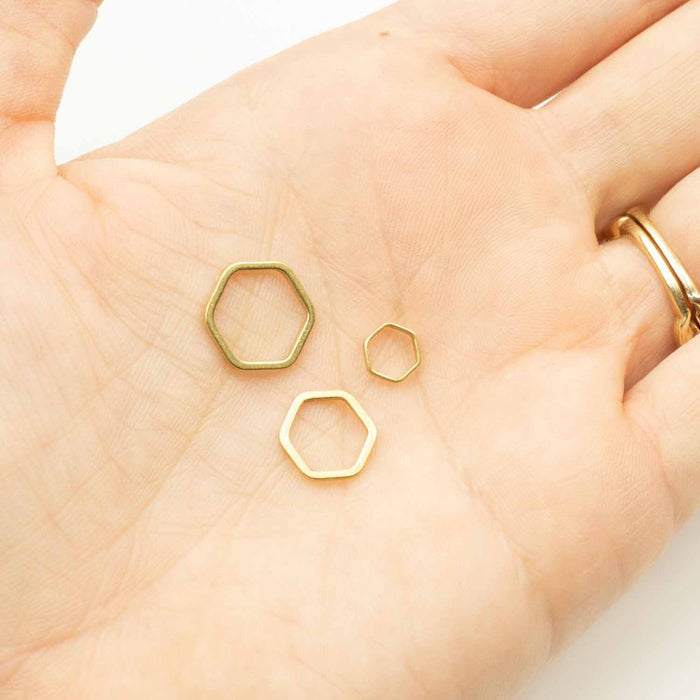 Hand holding three gold hexagonal honeycomb stitch markers in small medium and large sizes in palm to show scale