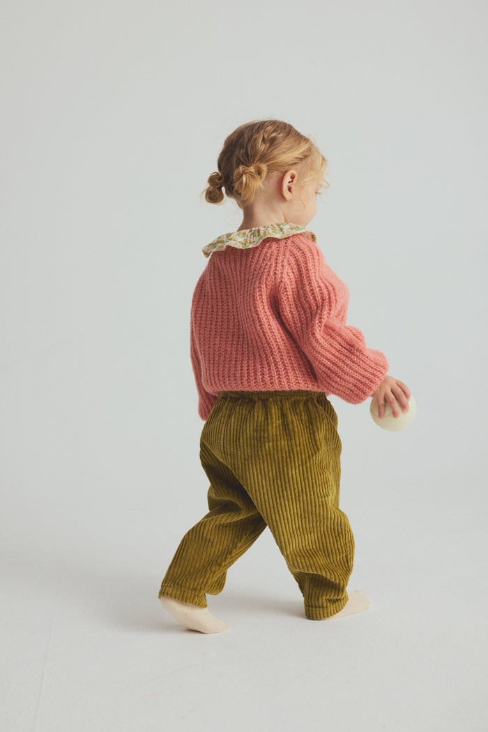 child wearing pink cardigan over collared shirt with corduroy pants on light grey background