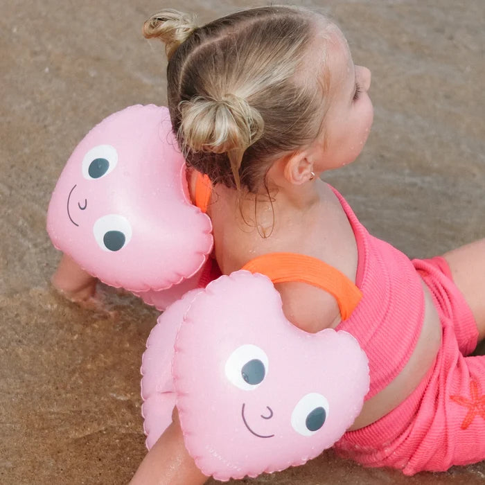 Child wearing pink inflatable arm floats on a sandy beach