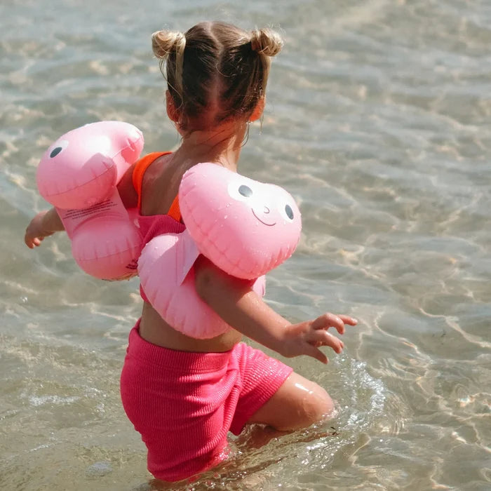 Child wearing pink inflatable arm floats in shallow water