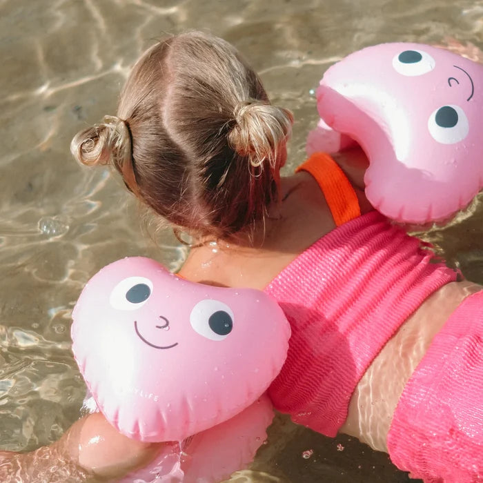 Child in pink swimsuit with pink heart-shaped floaties in water