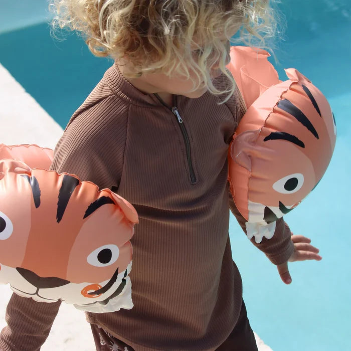 Child wearing tiger-themed inflatable arm floats by a pool