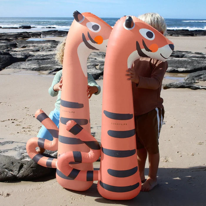 Two children holding large inflatable tiger toys on a beach.