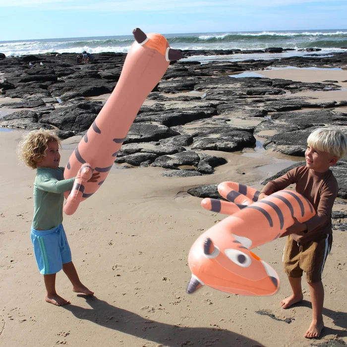 Two children playing with inflatable tiger toys on a rocky beach.