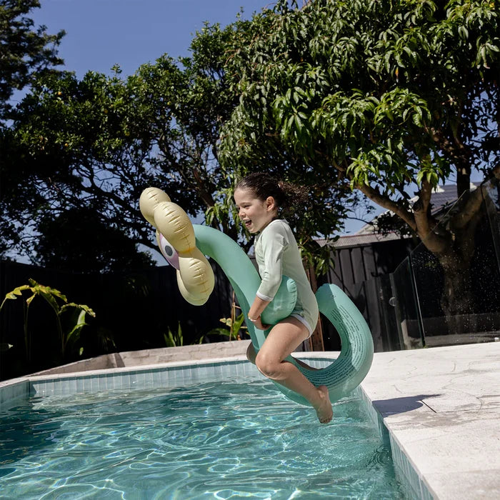 Child playing on a inflatable noodle by a pool with trees in the background