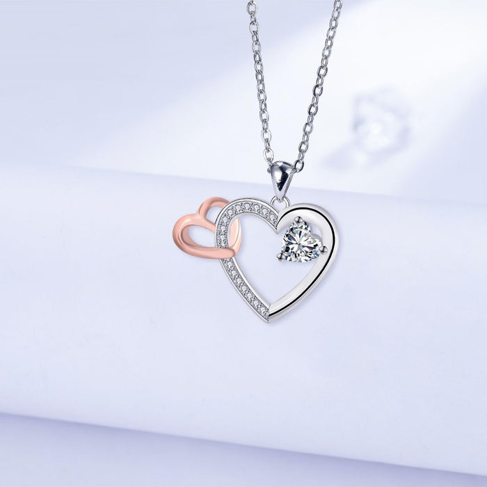 Elegant silver and rose gold interlocking heart pendant necklace with a brilliant heart-shaped crystal center stone.