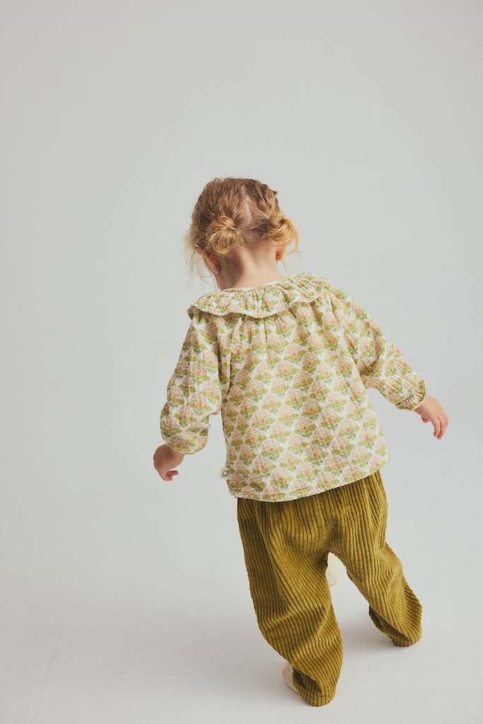child wearing green floral blouse and corduroy pants.