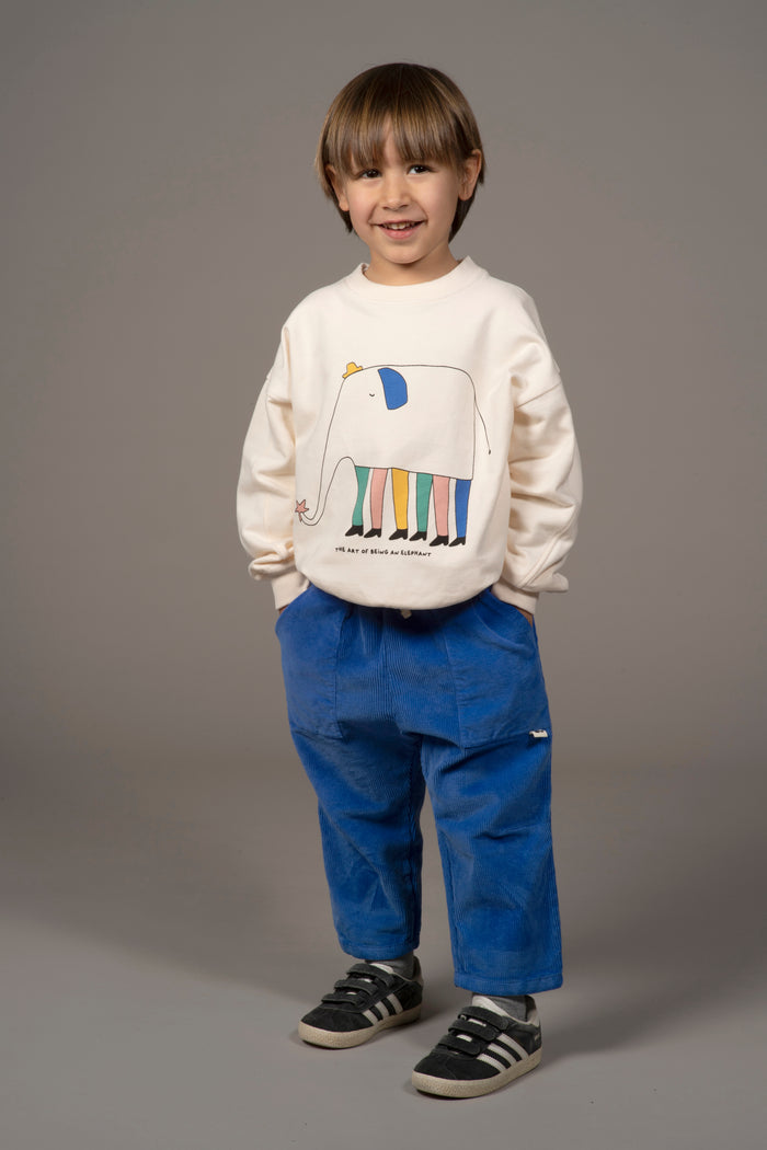 child modeling cream sweatshirt with illustrated elephant and blue corduroy pants on grey background