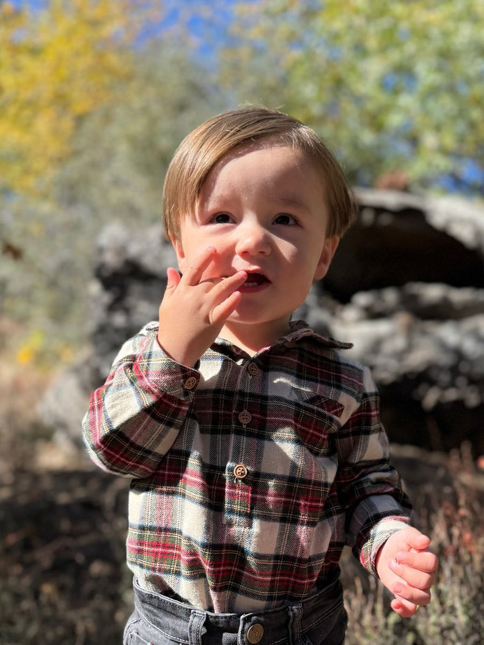 Child in a plaid shirt standing outdoors with trees in the background