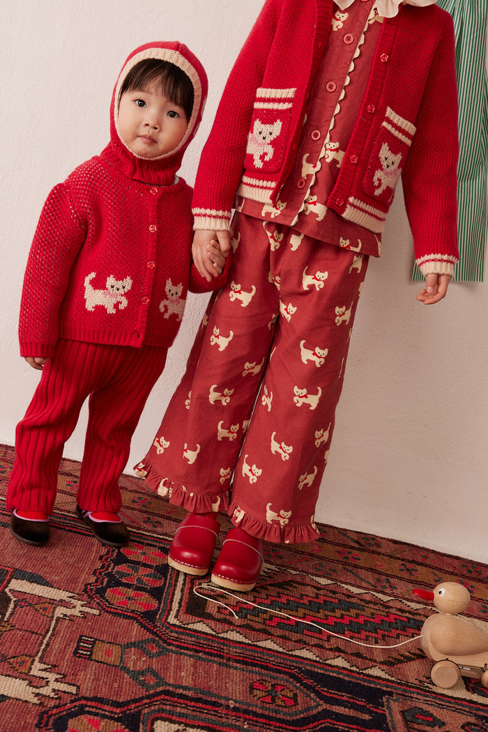 A toddler and an adult wearing matching red knit holiday sweaters and pants sets with cream cat motifs, standing on a patterned rug indoors.